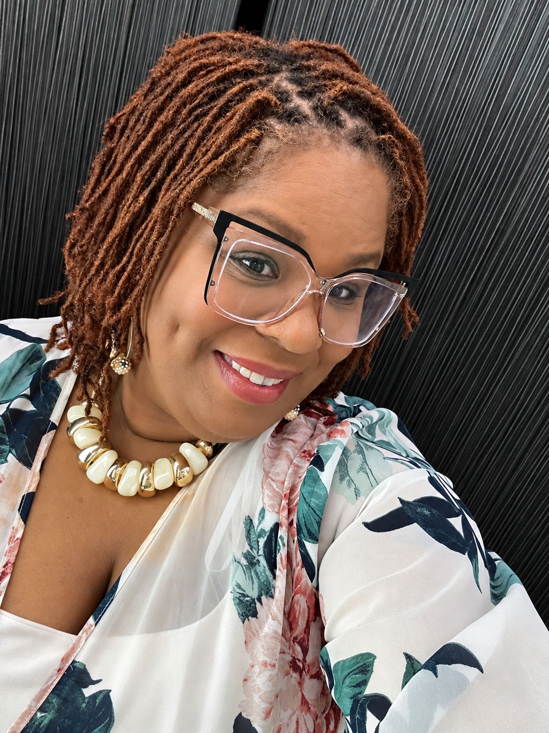 Kemi Miller smiling, wearing clear cat-eye glasses and a pearl and gold necklace